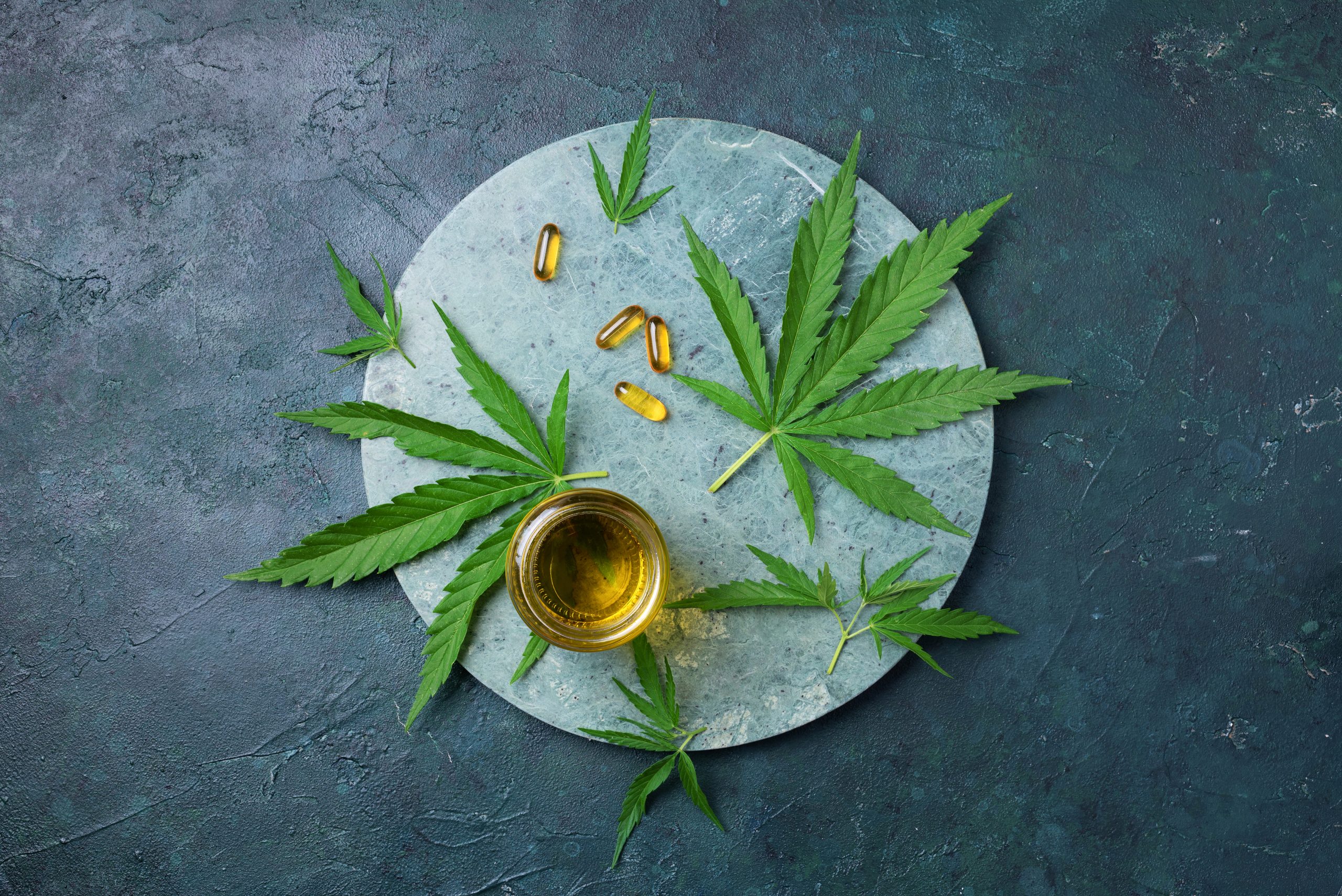 CBD oil, hemp oil capsules and cannabis leaves on dark background. Flat lay, copy space. Cosmetics CBD oil. Alternative medicine. Natural supplements, treatment CBD oil, hemp oil capsules and cannabis leaves on dark background. Flat lay, copy space. Cosmetics CBD oil. Alternative medicine. Natural supplements, treatment.
